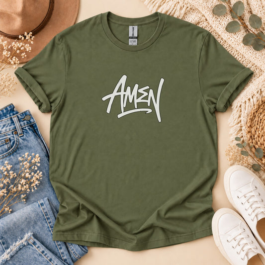 Olive green t-shirt with white "AMEN" graphic, laid flat with jeans, hat, and sneakers.