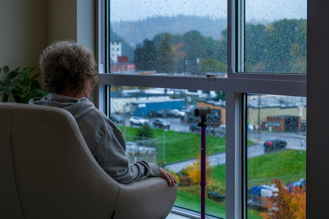 A woman sits quietly by a rainy window in a private moment of grief and remembrance, reflecting the quiet season after losing a spouse — Nordenzi