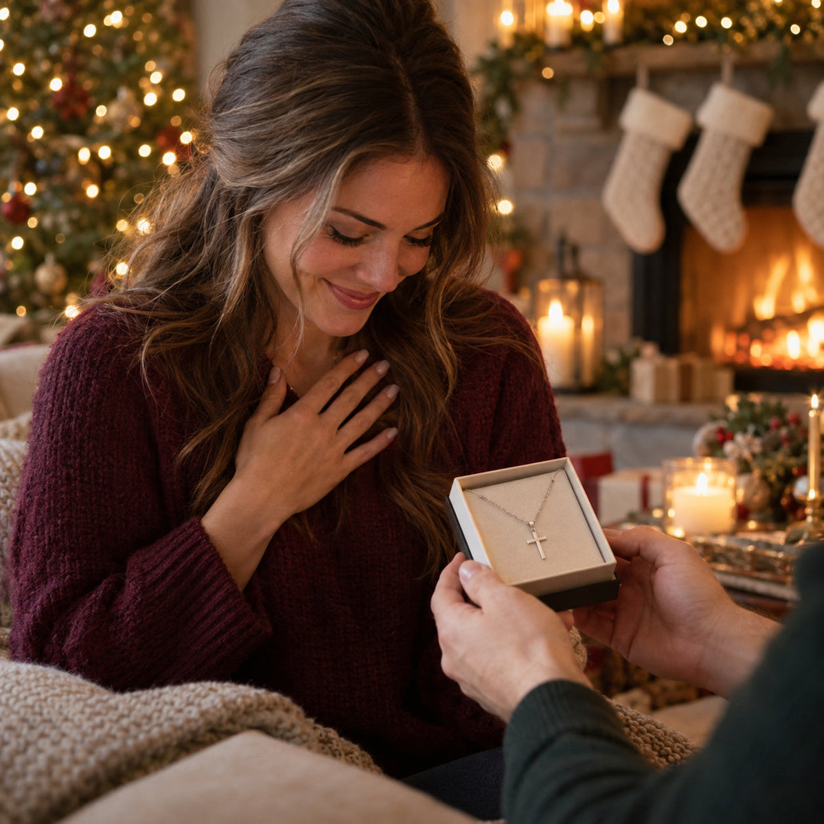 Wife smiling by the fireplace as her husband hands her a silver cross necklace gift box – Christian Christmas gifts for wife