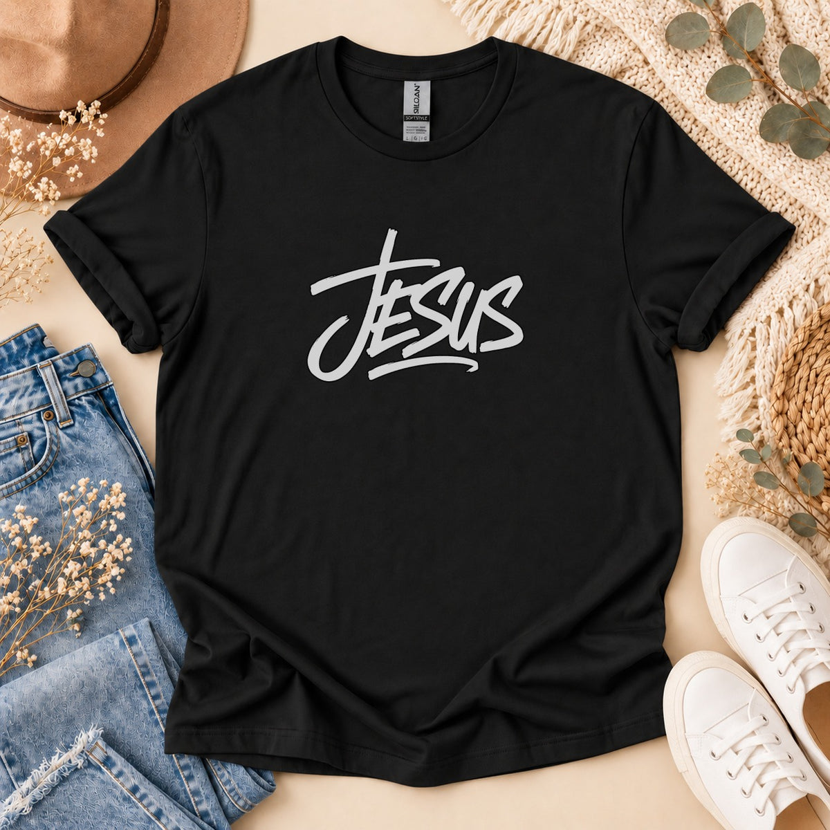Black t-shirt with white "Jesus" graphic, laid flat with jeans and sneakers.