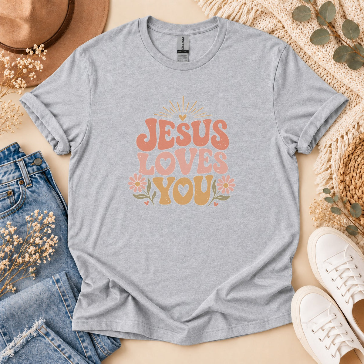 Grey t-shirt with "Jesus Loves You" graphic in retro font and pastel colors.