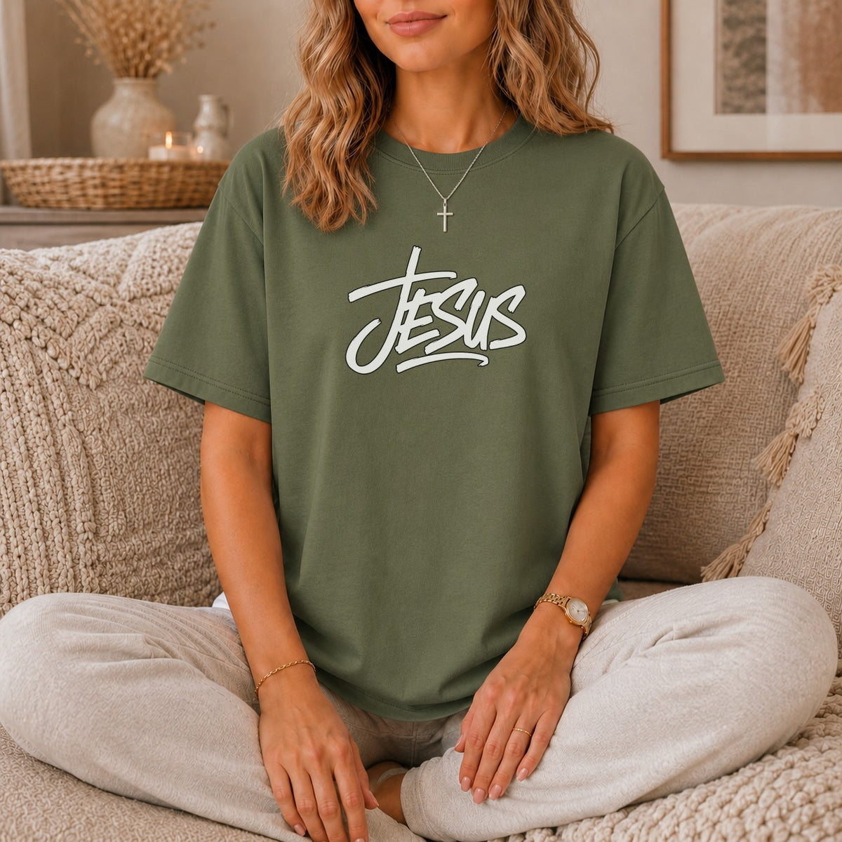 Olive green t-shirt with white "Jesus" script graphic, worn by a seated woman.