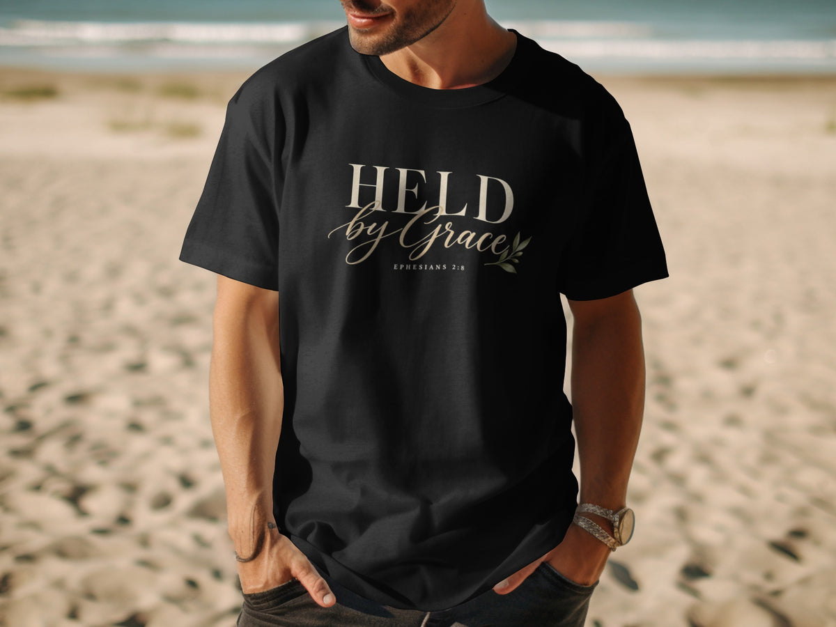 Black t-shirt with "HELD by Grace" and Ephesians 2:8 text, person on a beach.