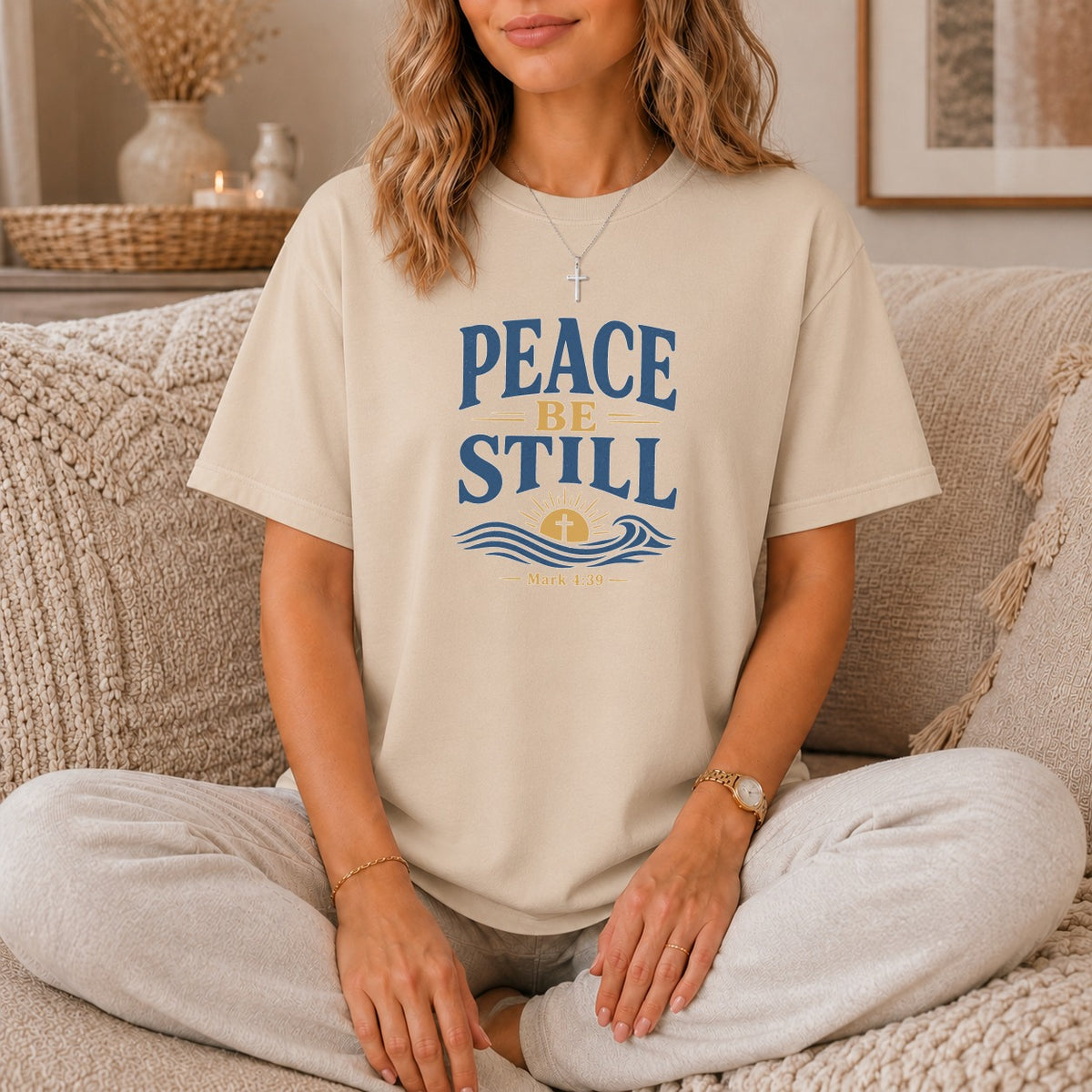 Beige t-shirt with "PEACE BE STILL" text and a sunrise over waves graphic.