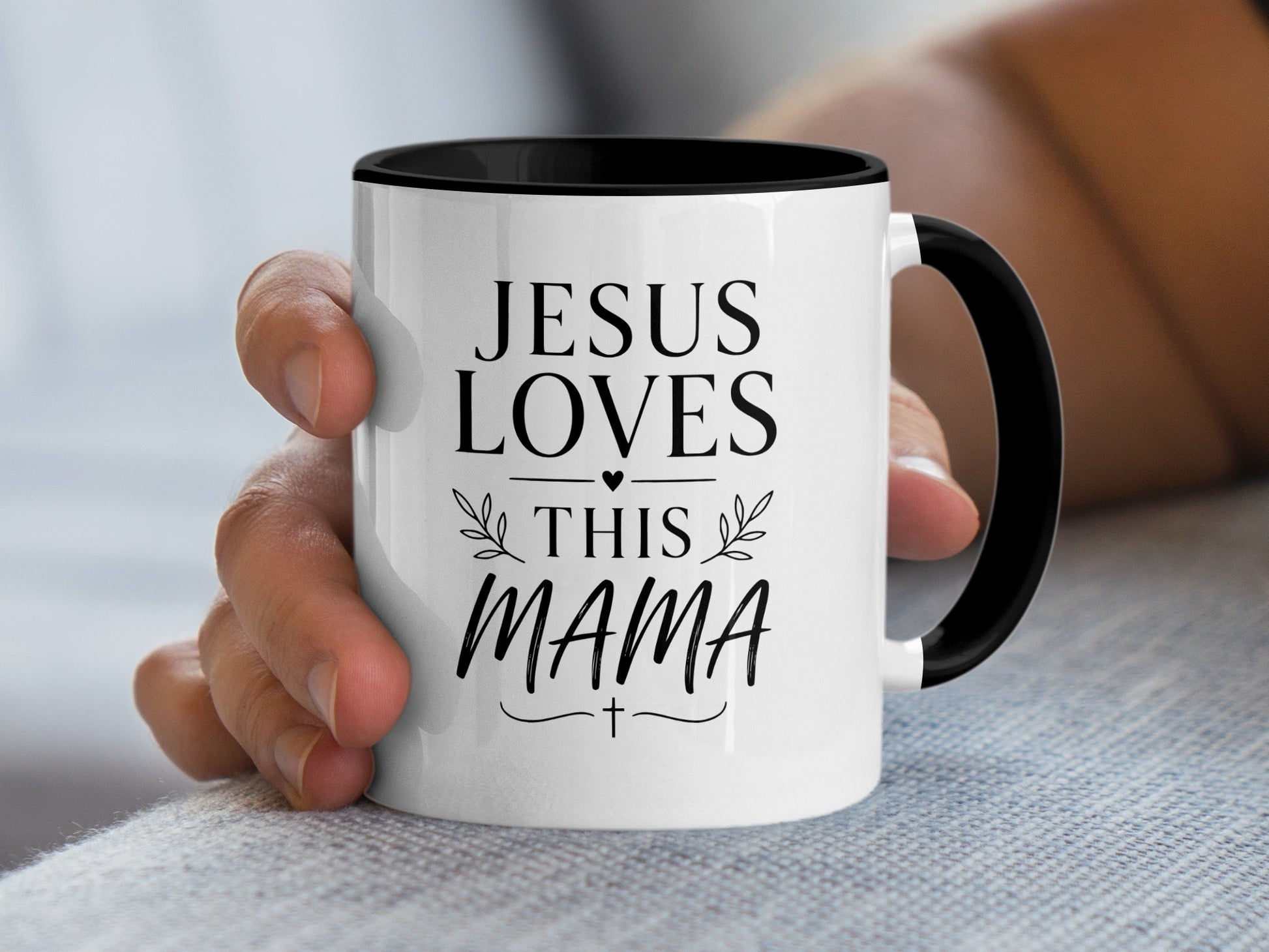 White mug with black rim and handle, saying "Jesus Loves This Mama" with a cross.