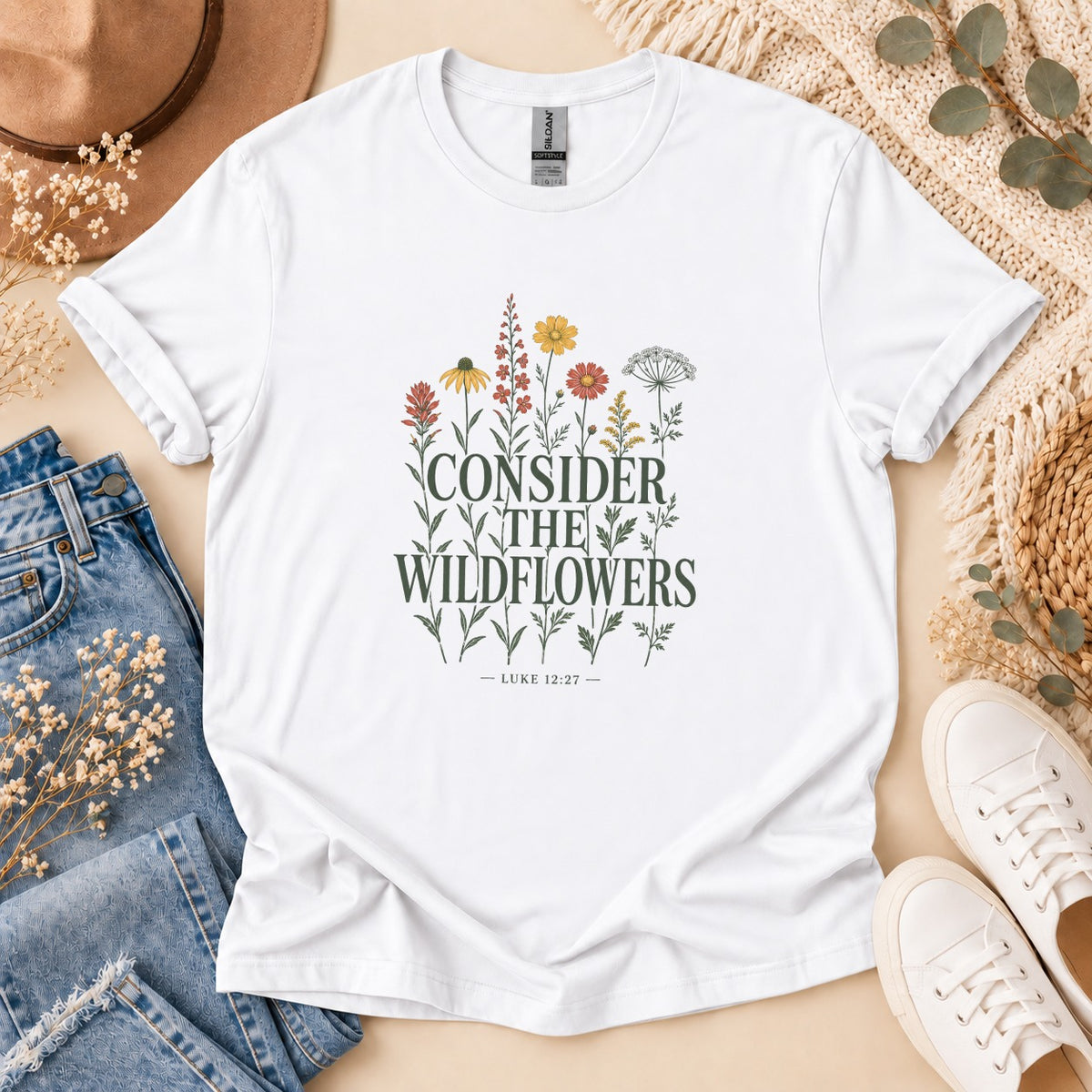 White t-shirt with "CONSIDER THE WILDFLOWERS" and "LUKE 12:27" text, surrounded by flowers.