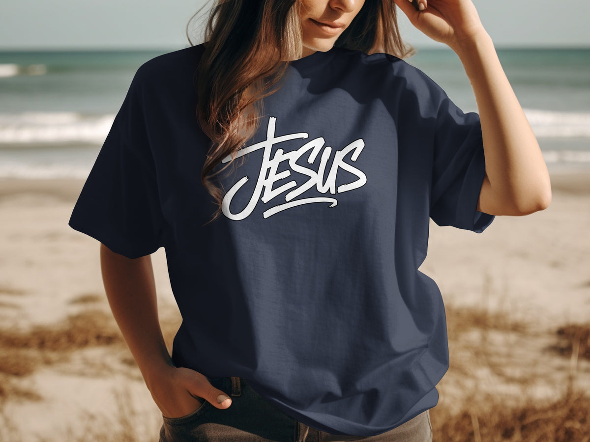Navy t-shirt with white "JESUS" text graphic on beach background.