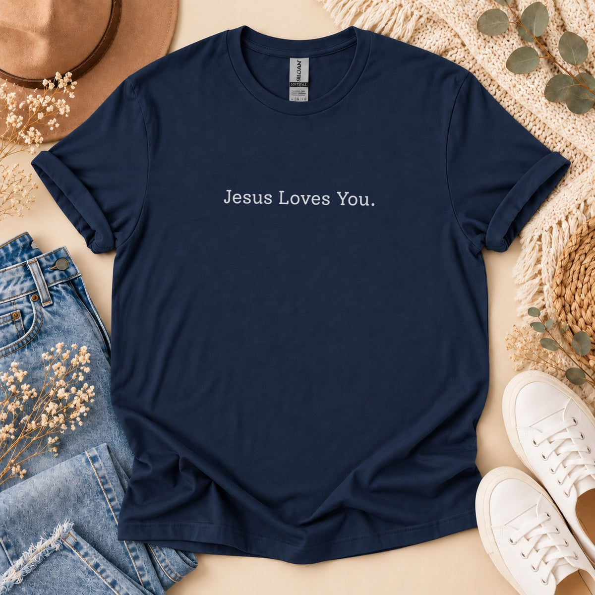 Navy blue t-shirt with "Jesus Loves You." text, flat lay with jeans and sneakers.