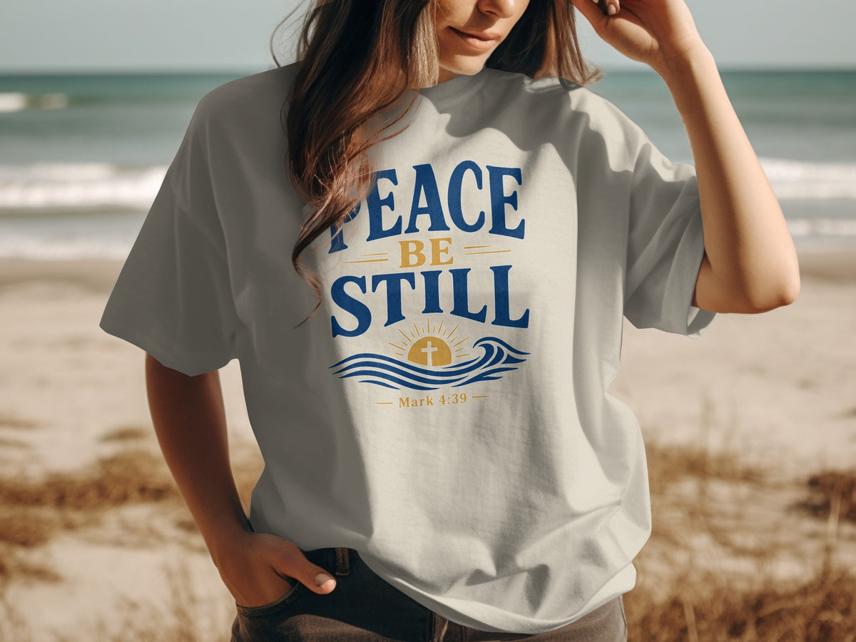 T-shirt with "Peace Be Still" text, cross, sun, and waves graphic.