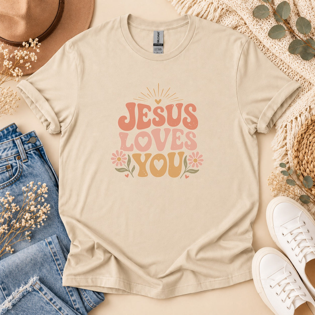 Beige t-shirt with "JESUS LOVES YOU" text in retro font and floral accents.